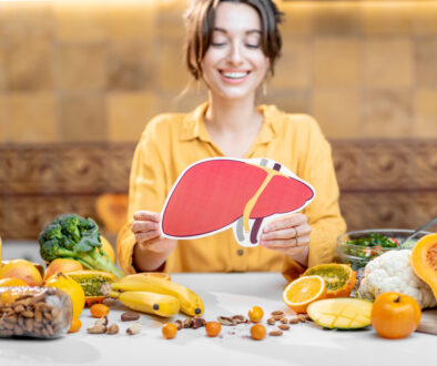 Woman Smiling and Holding a Model of a Human Liver at a Table Full of Healthy Foods Can Fatty Liver Disease Be Reversed