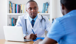 An African American Doctor Sitting at a Desk Listening Intently to a Patient Who Should See an Internist